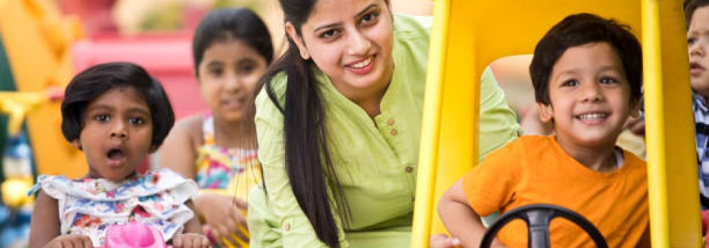 Teacher with preschool students enjoying toy rides at playground